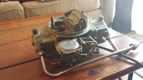 1995 Ford Bronco - A carburetor sits on a wooden table, with a couch visible behind it.