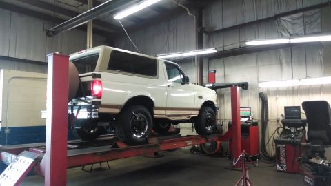 1994 Ford Bronco - A white 1994 Ford Bronco is shown on a vehicle lift inside a garage, likely undergoing maintenance or inspection.