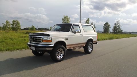 1994 Ford Bronco - White 1994 Ford Bronco with tan trim parked on the side of a road under a cloudy sky.