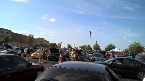 2004 Ford Crown Victoria - A gathering of vehicles and people in a parking lot under a bright blue sky.