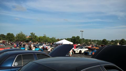 2004 Ford Crown Victoria - Wide view across an outdoor car show in a paved lot, with rows of parked cars, open hoods, and a white pop-up canopy under a partly cloudy…