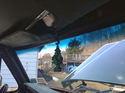 1979 Ford Bronco - View from inside a vehicle shows an air freshener and the open hood, with a house and yard visible outside.
