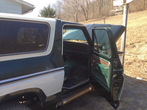 1979 Ford Bronco - The interior of a 1979 Ford Bronco, green upholstery and wood-grain trim, is visible with both doors ajar.