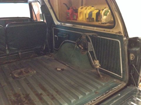1979 Ford Bronco - The rear cargo area of an older vehicle shows a floor with ribbed metal and a shelf stocked with various containers of liquid.