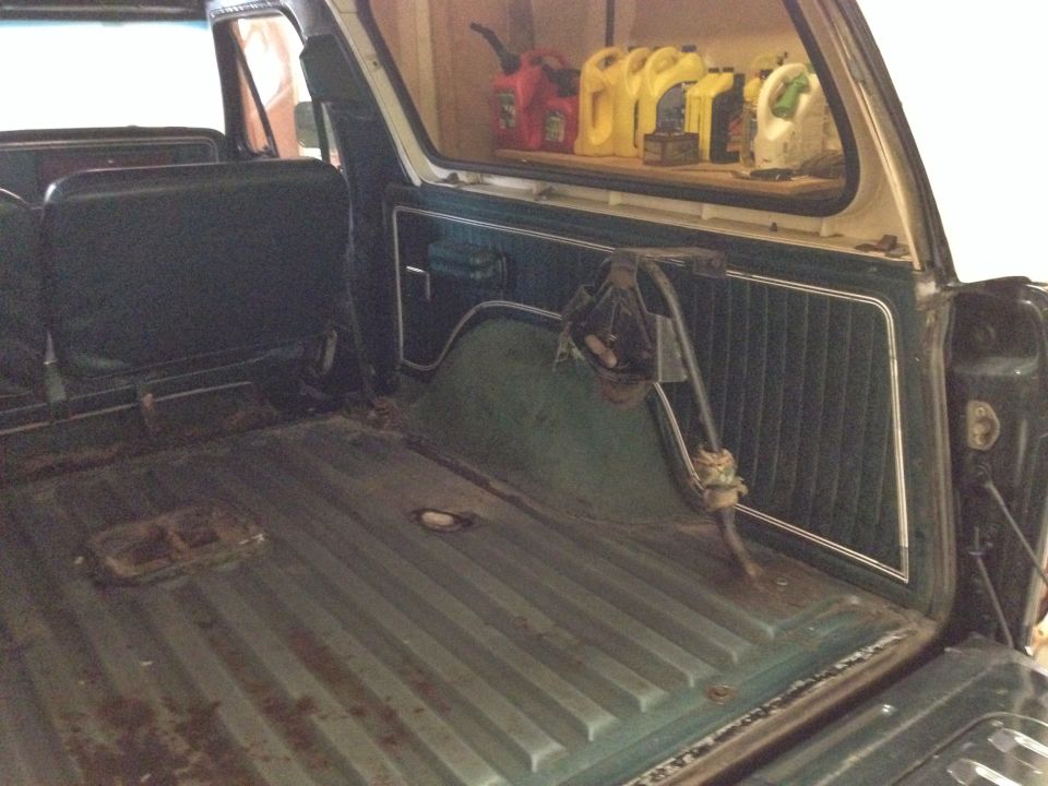 Interior cargo area of a vehicle with dark green seats and floor, and a shelf with several yellow and red gas cans in the background