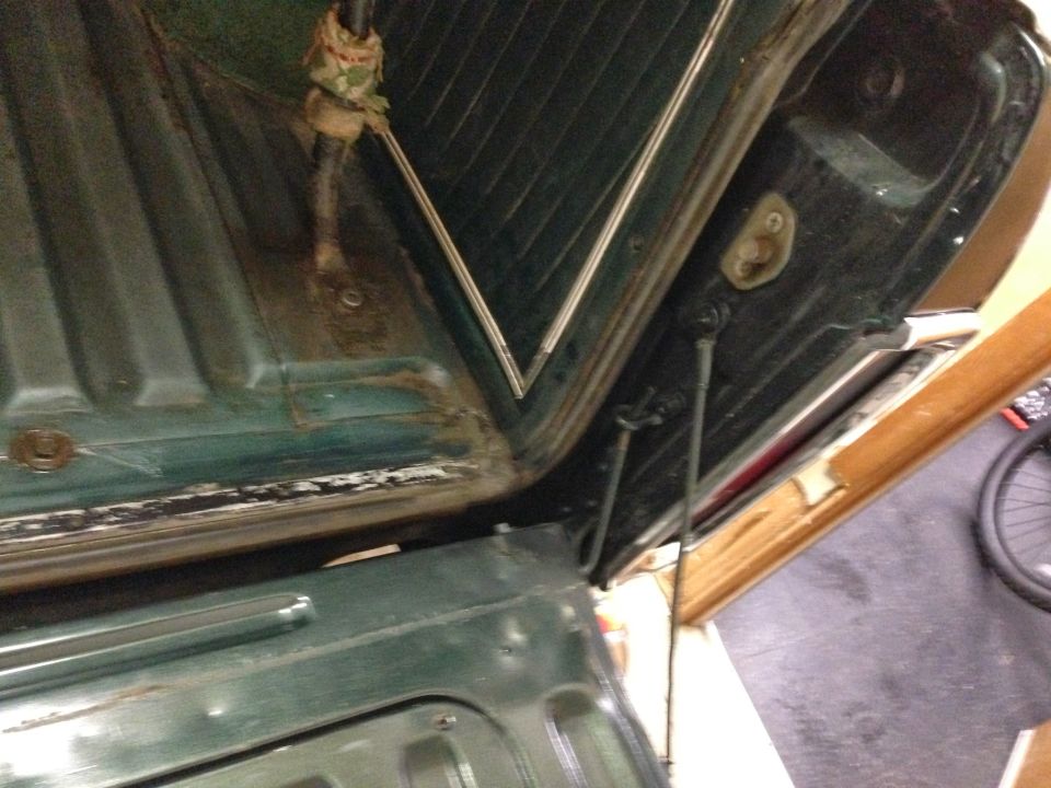 Green interior of a 1978 Ford Bronco with visible rust and dirt around the tailgate hinges