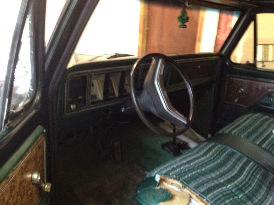 Green striped seat with torn upholstery, dark dashboard with rectangular gauges, and a two-spoke steering wheel