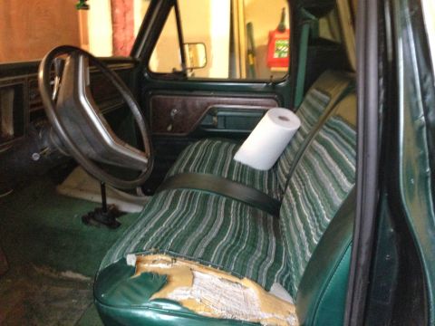 1979 Ford Bronco - The interior of a 1979 Ford Bronco shows green striped seats with a torn driver's side cushion and a roll of paper towels on the passenger…