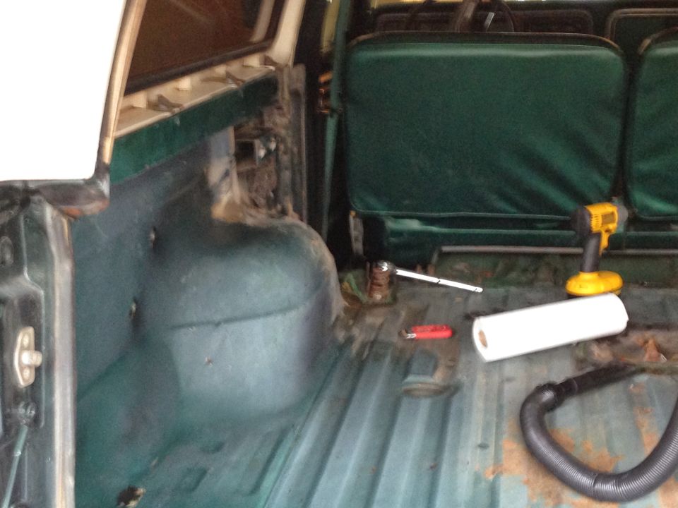 Green interior of a 1978 Ford Bronco with a roll of paper towels, a drill, and a vacuum hose