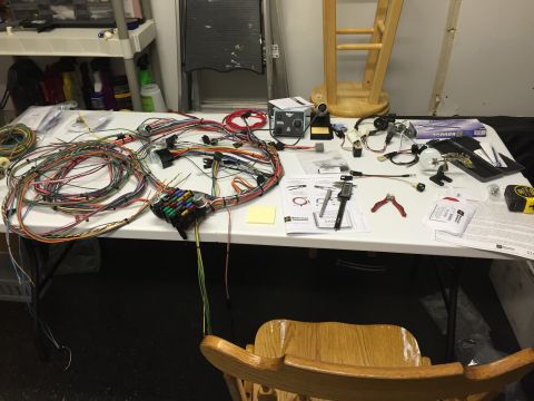 1979 Ford Bronco - A table is covered with a complex wiring harness, fuse box, various tools including a soldering iron, wire strippers, and a digital caliper…