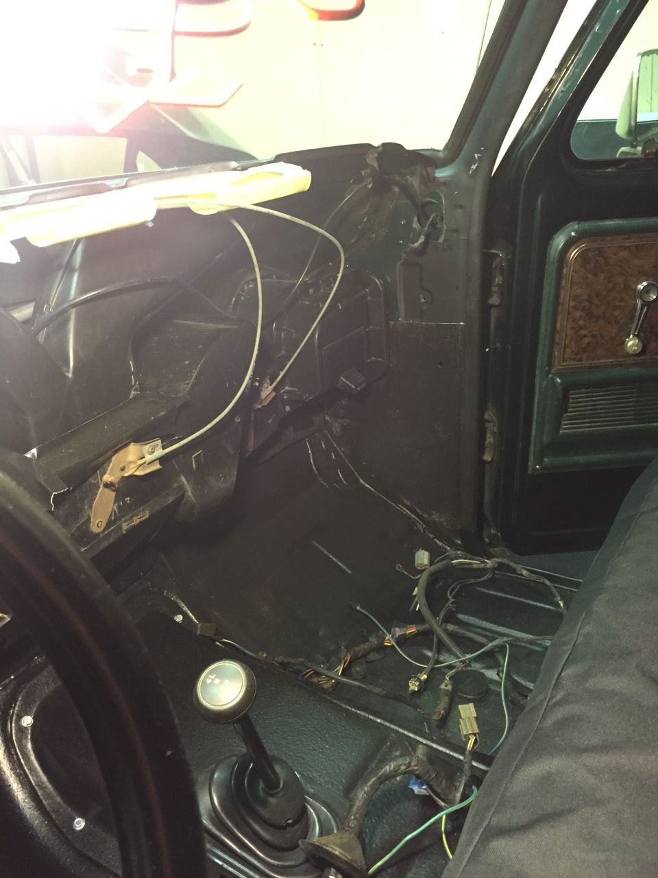 Interior of a vintage vehicle showing dashboard, floor, shifter, and door panel with woodgrain trim.