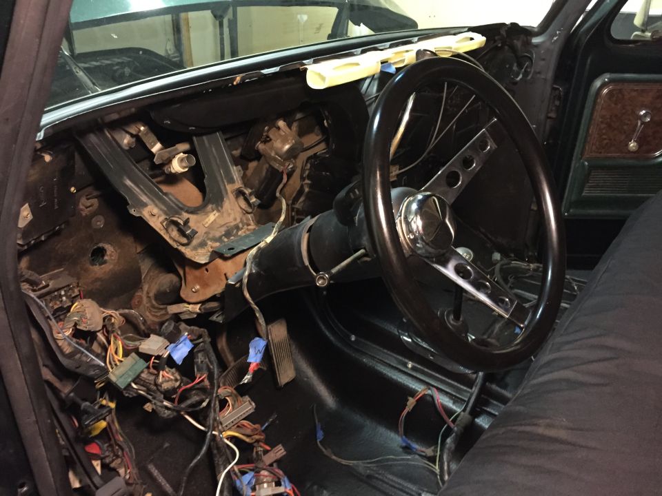 Interior view of a classic Bronco dashboard with exposed wires, steering wheel, and pedals.