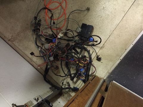 1979 Ford Bronco - A tangled mess of automotive wiring harnesses and a black electronic control unit are laid out on a concrete floor. The wiring includes ora…