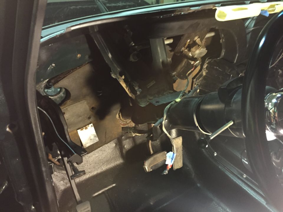 Interior of a classic vehicle showing dashboard, steering column, pedals, and wiring.