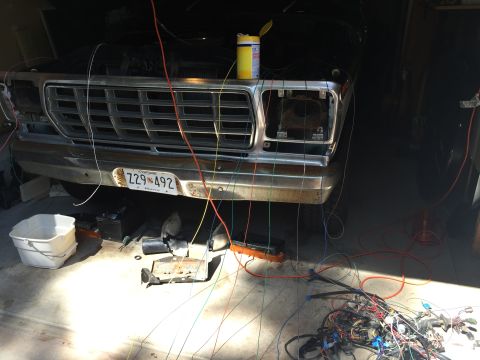 1979 Ford Bronco - The front end of a classic pickup truck, possibly a 1979 Ford Bronco, is shown with its hood open and a complex wiring harness laid out in…