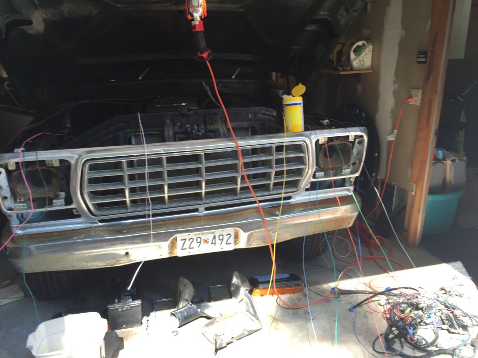 Front of a classic Ford truck or SUV with hood open, showing extensive wiring work.