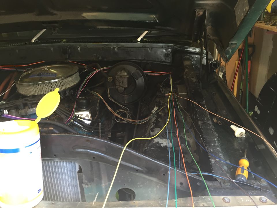 Engine bay of a vintage Ford Bronco with many colorful wires and an air filter.
