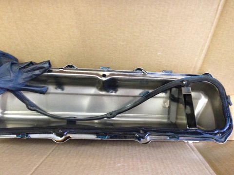 1979 Ford Bronco - A chrome valve cover with a black gasket is laid out on a cardboard surface. A blue glove is partially visible on the left side of the valv…
