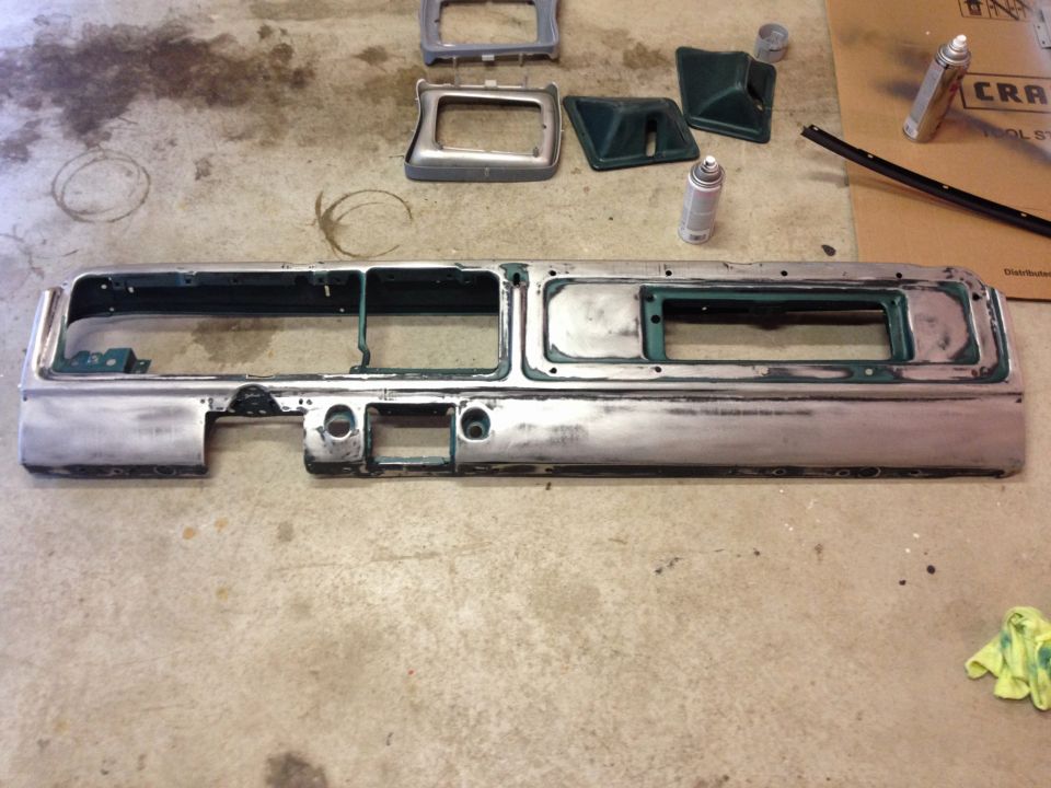 Silver dashboard panel with cutouts, green trim pieces, and spray cans on concrete floor.