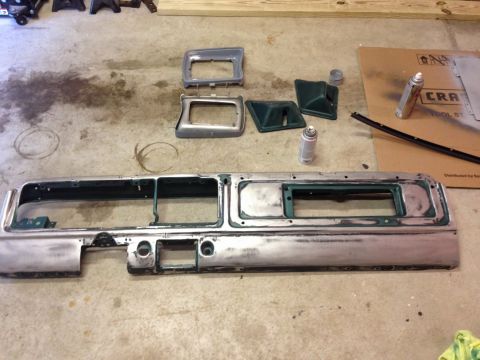 1979 Ford Bronco - A collection of vintage car dashboard parts, including a large metallic trim piece, are laid out on a concrete floor. Several spray cans an…