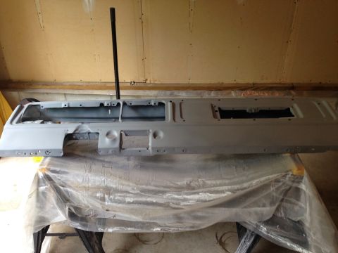 1979 Ford Bronco - A gray, primed dashboard assembly is laid out on a workbench covered with plastic sheeting. The dashboard has cutouts for instruments and a…