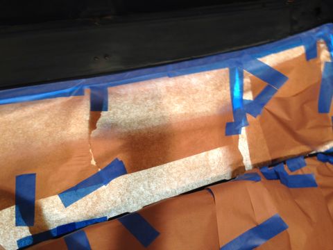 1979 Ford Bronco - Blue painter's tape and brown paper are used to mask off an area above a dark surface, likely for painting or protection. The tape is appli…