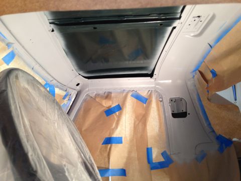 1979 Ford Bronco - Interior view of a vehicle undergoing painting, with masking paper and blue painter's tape covering various surfaces. A large, dark-colored…