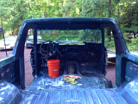1979 Ford Bronco - The interior of a disassembled dark green 1979 Ford Bronco is shown from the rear, with the doors removed and the bed stripped down to prim…