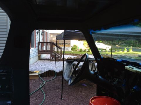 1979 Ford Bronco - View from inside a vehicle looking out at a backyard. The interior shows a steering wheel and dashboard with exposed wiring, while the exte…
