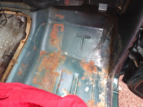1979 Ford Bronco - The interior floor pan of a vintage vehicle, likely a 1979 Ford Bronco, shows significant rust and corrosion. A red fabric item is visible…