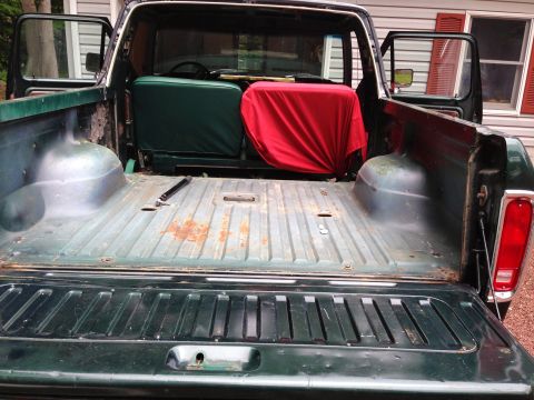 1979 Ford Bronco - The open tailgate of a dark green pickup truck reveals the bed, which contains two seat cushions, one green and one red. A black tool is ly…