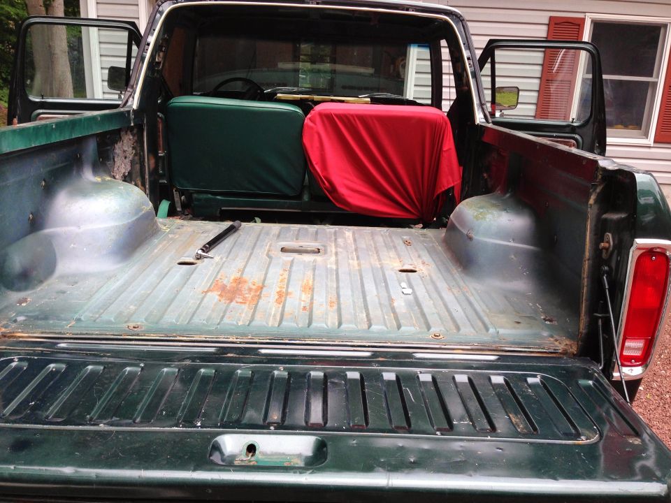 Rear view of a dark green pickup truck with tailgate down, showing the bed with green and red seat cushions.