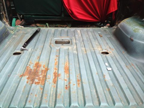 1979 Ford Bronco - The interior of a vintage vehicle's cargo area shows a ribbed, teal-colored metal floor with significant rust spots. A black socket extensi…