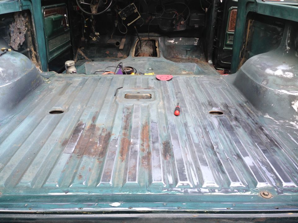 Interior of a vintage Ford Bronco with stripped floor, showing rust and tools.