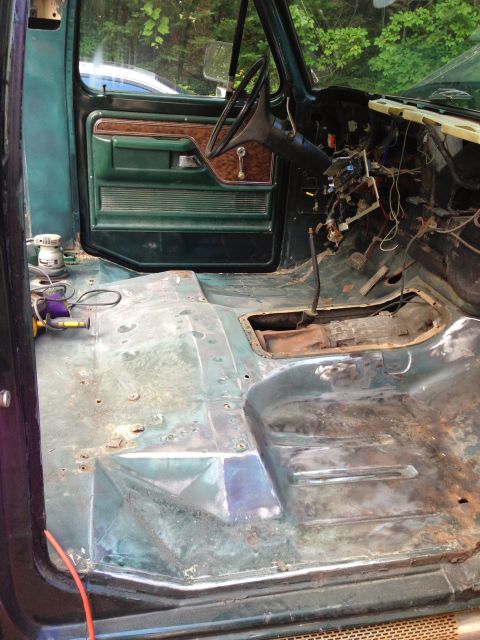 1979 Ford Bronco - The interior of a vintage Ford truck or SUV is shown with the floor pan stripped down to bare metal, revealing rust and previous repairs. T…