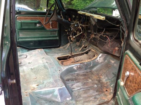 1979 Ford Bronco - The interior of a vintage Ford Bronco is shown with the floor pan exposed and showing signs of rust and repair. The dashboard and door pane…
