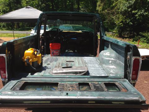 1979 Ford Bronco - The rear view of a vintage green pickup truck bed with the tailgate down, showing a yellow shop vac and an orange bucket. The truck appears…