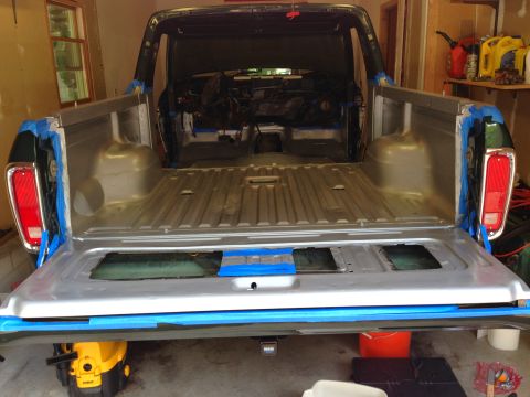 1979 Ford Bronco - The open tailgate of a dark green pickup truck bed is shown, with the interior of the bed appearing to be prepped for painting. Blue painte…