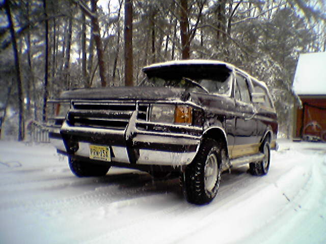 Dark Ford Bronco with brush guard covered in snow in a wooded driveway