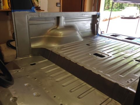 1979 Ford Bronco - The interior of a vehicle's bed and cabin floor has been stripped and appears to be prepped for painting. The metal floor shows ribbed sect…