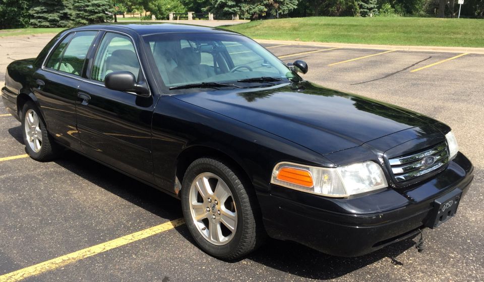 Black 2007 Ford Crown Victoria sedan, front passenger side view, parked in a lot.