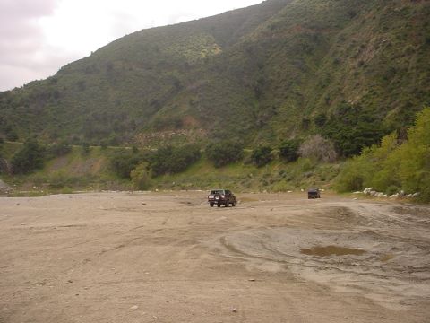 1988 Ford Bronco - Two SUVs navigate a dusty, mountainous terrain under an overcast sky.