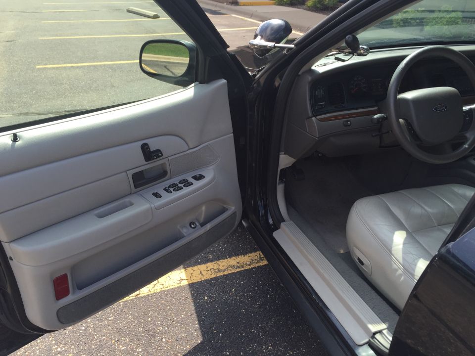 Interior of a dark sedan, driver's side door open, showing door panel, dashboard, steering wheel, and seat.