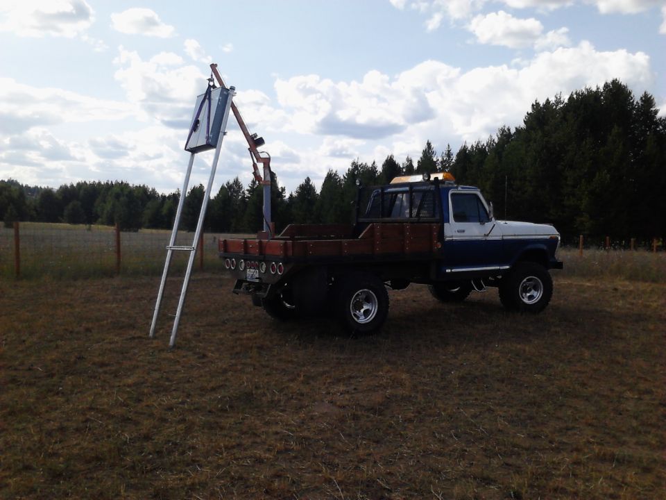 Blue and white Ford flatbed truck with crane attachment parked in a field.