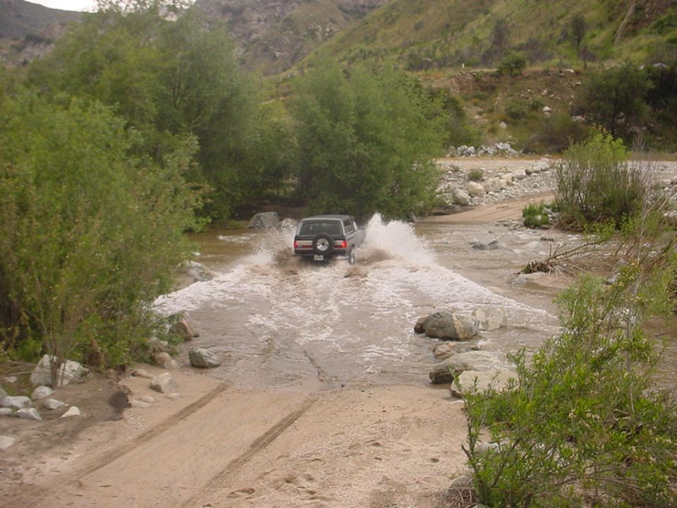 Dark SUV with rear spare tire splashing through a muddy river crossing in a canyon wash