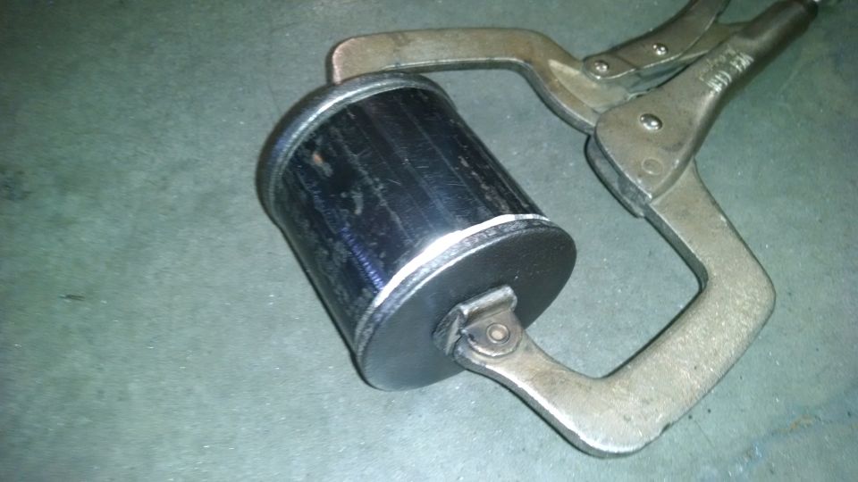 Black cylindrical object with silver end caps held by a C-clamp on a gray surface.