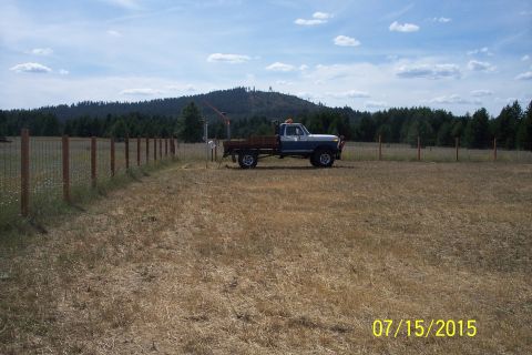 1989 Ford Bronco - A blue and white pickup truck with a wooden flatbed is parked in a dry, grassy field with a wooded hill in the background. A fence runs alo…