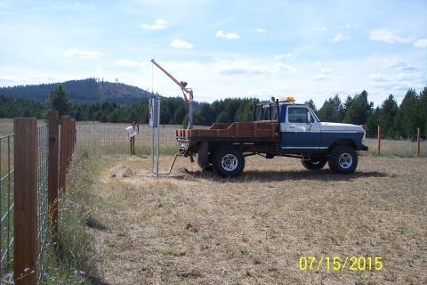 1989 Ford Bronco - A blue and white flatbed pickup truck with a wooden bed is parked in a dry, grassy field next to a fence. A metal pole with some equipment…