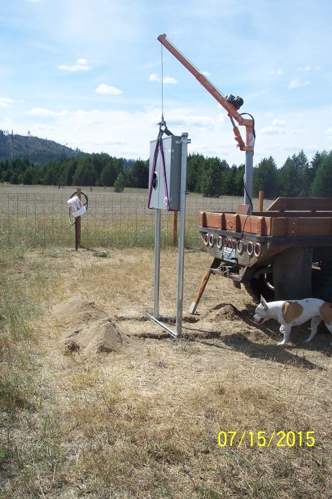 1989 Ford Bronco - A utility box is being lowered by a crane mounted on the back of a flatbed truck. A dog stands nearby in a dry, grassy field with trees in…