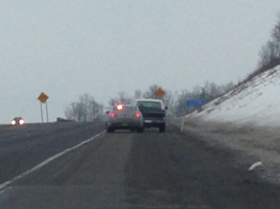 A pickup truck follows a sedan on a wet road in snowy conditions.